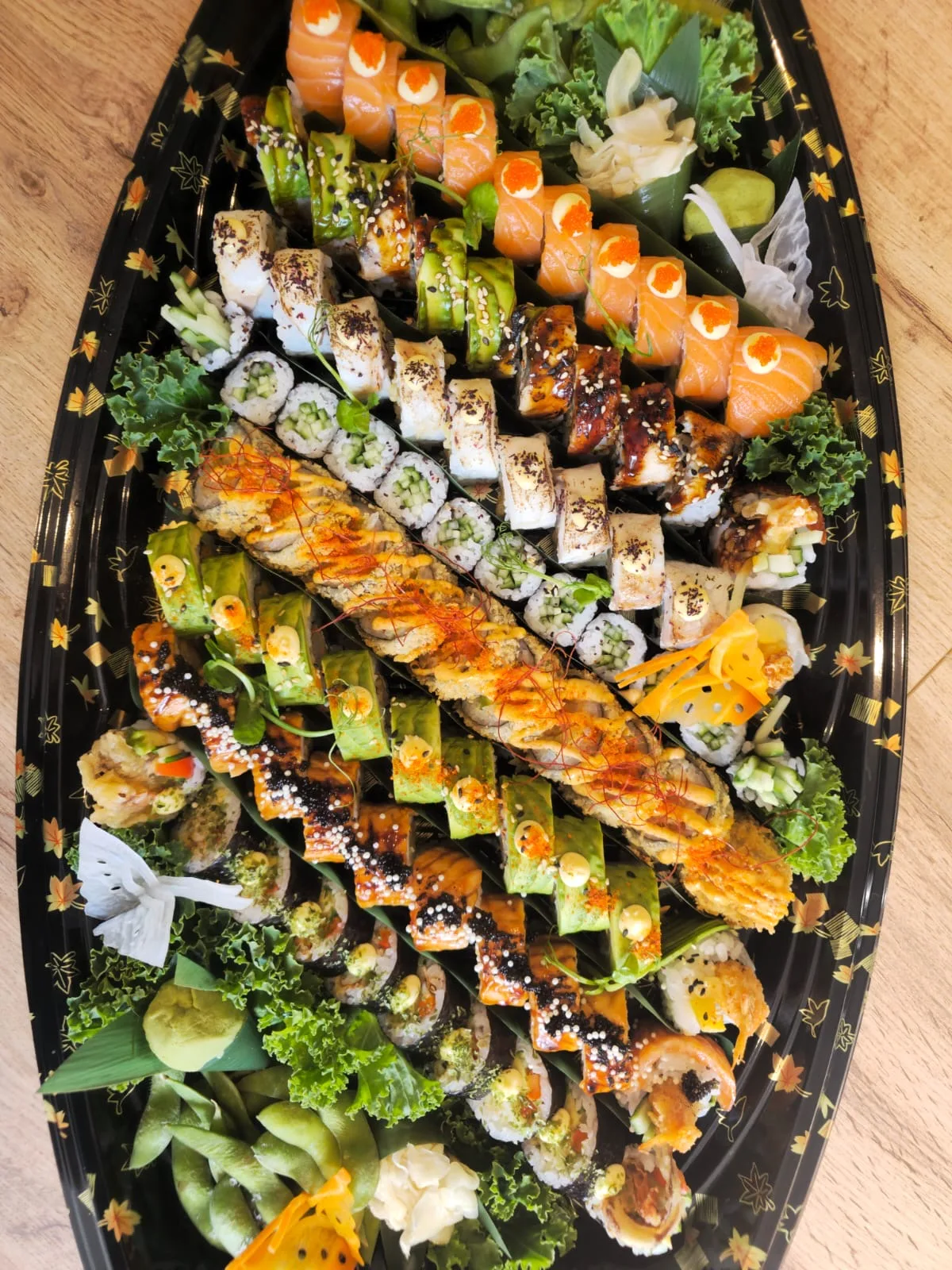 Party Platter on a black boat tray: salmon rolls topped with tobiko, avocado-wrapped rolls, eel-glazed rolls, cucumber maki and a tempura roll dressed with spicy mayo and chilli threads, with edamame, ginger and wasabi