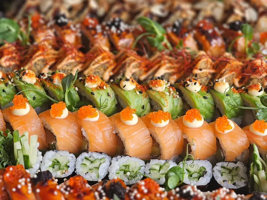 Close-up of a finished platter: salmon nigiri topped with roe, avocado rolls, cucumber maki and katsu rolls in tight rows